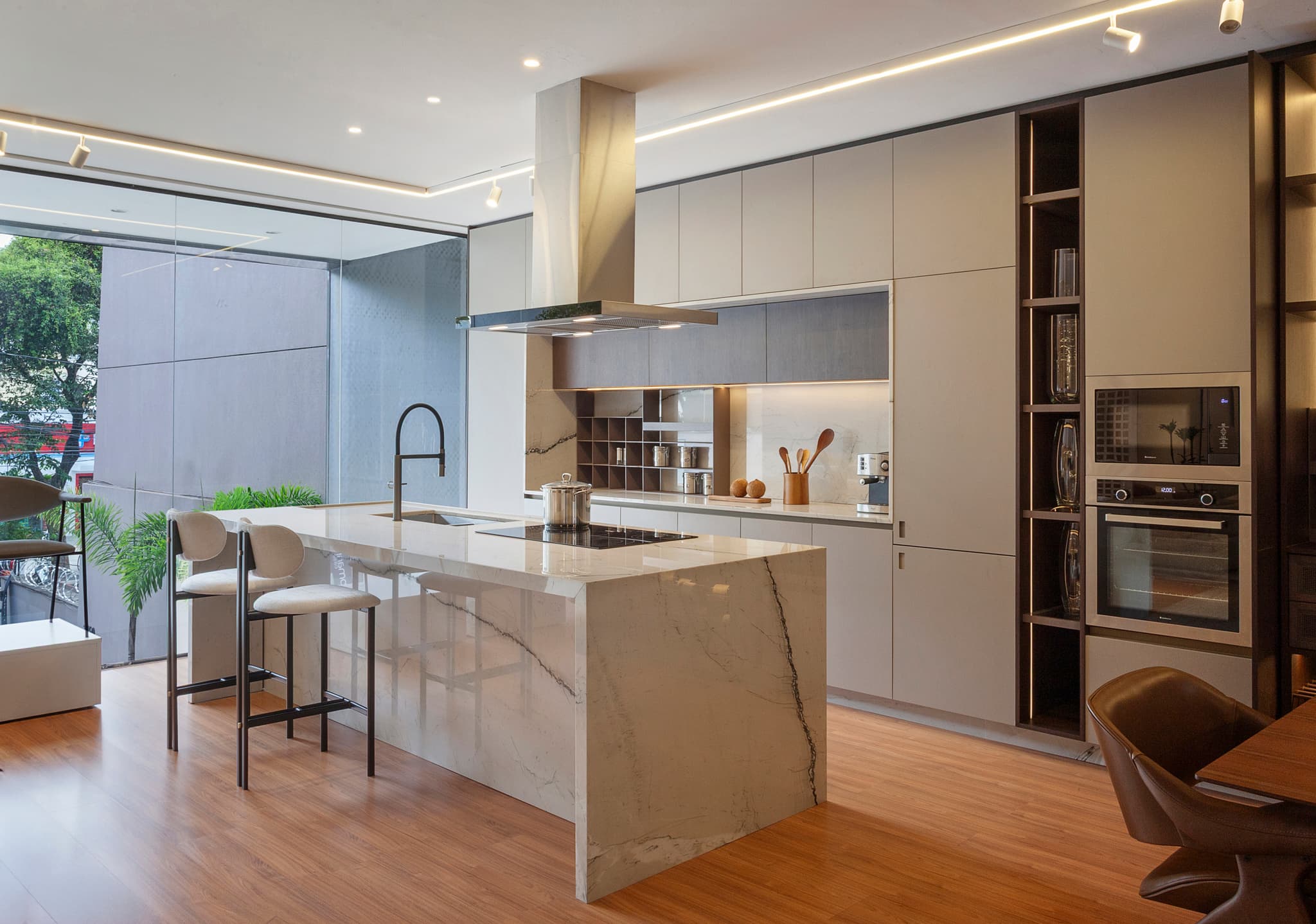 Cozinha planejada com ilha em mármore, banquetas e coifa suspensa